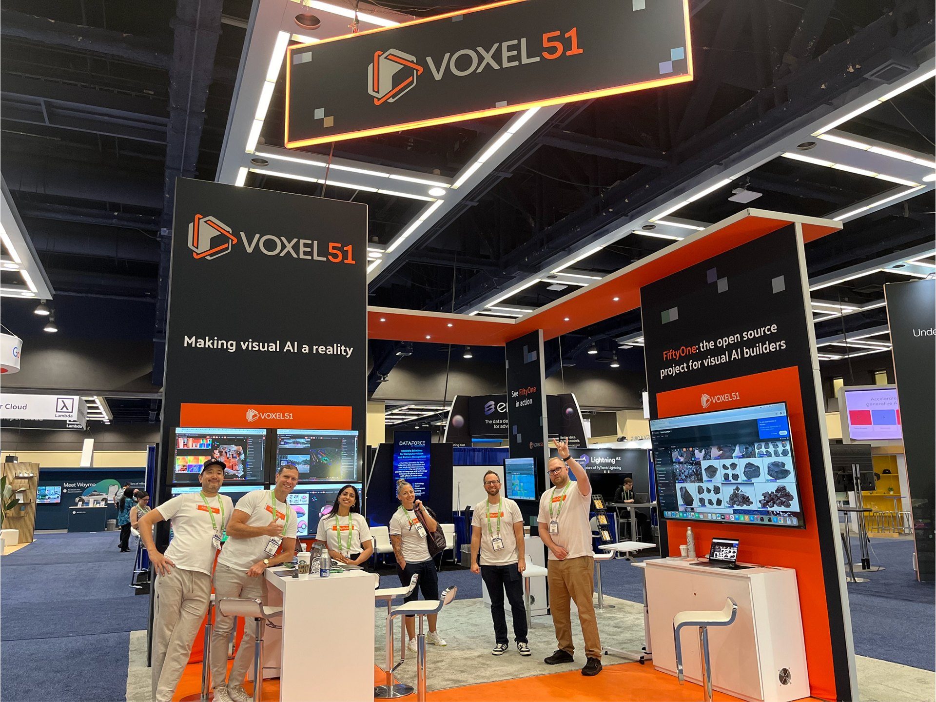 Voxel51 booth at CVPR 2024 with a lit hanging sign, black and orange towers, demo screens, and the team in event shirts