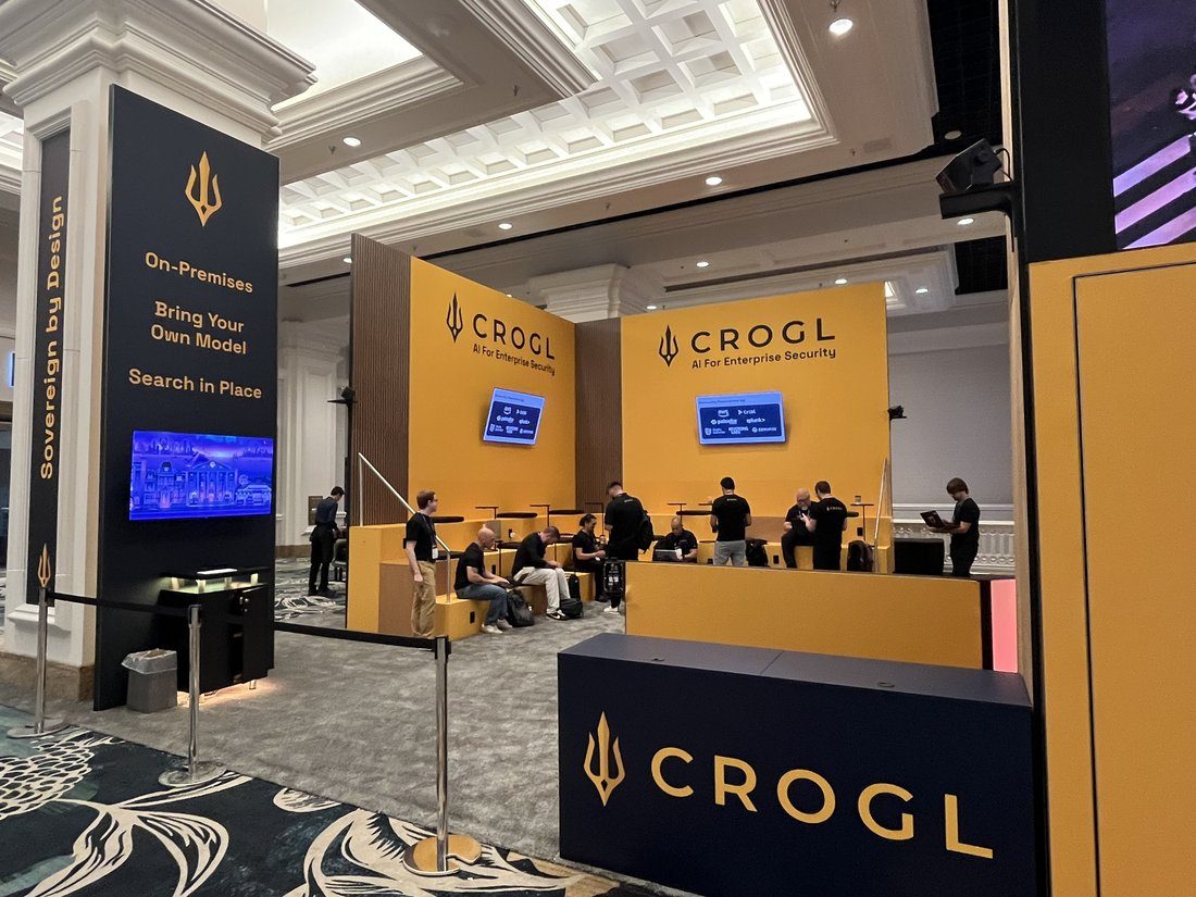 Crogl lounge in use, with attendees working on laptops on the tiered seating beneath the logo walls