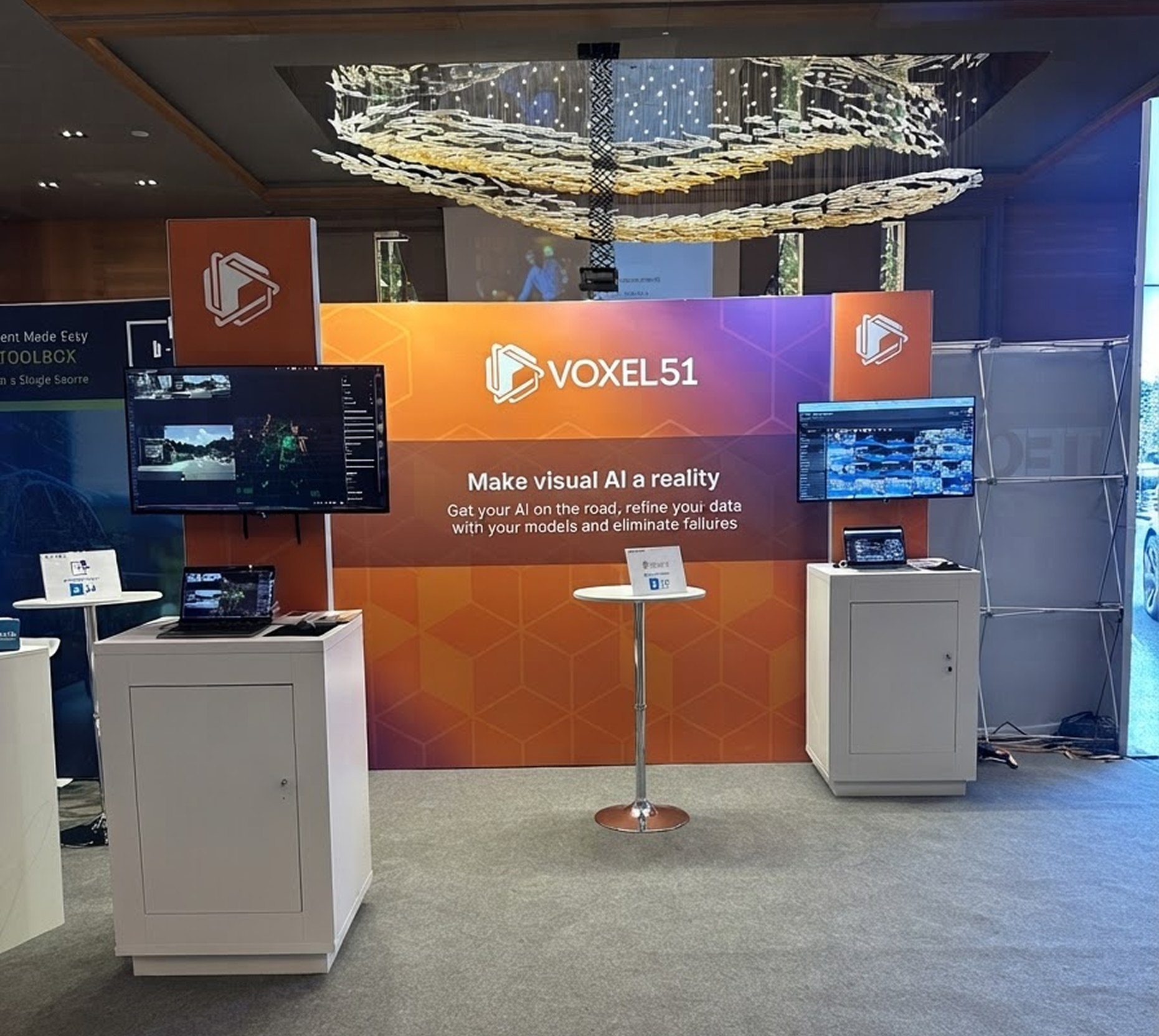 Voxel51 booth in the refreshed orange and purple gradient style, with the Make visual AI a reality headline, demo screens, and white counters